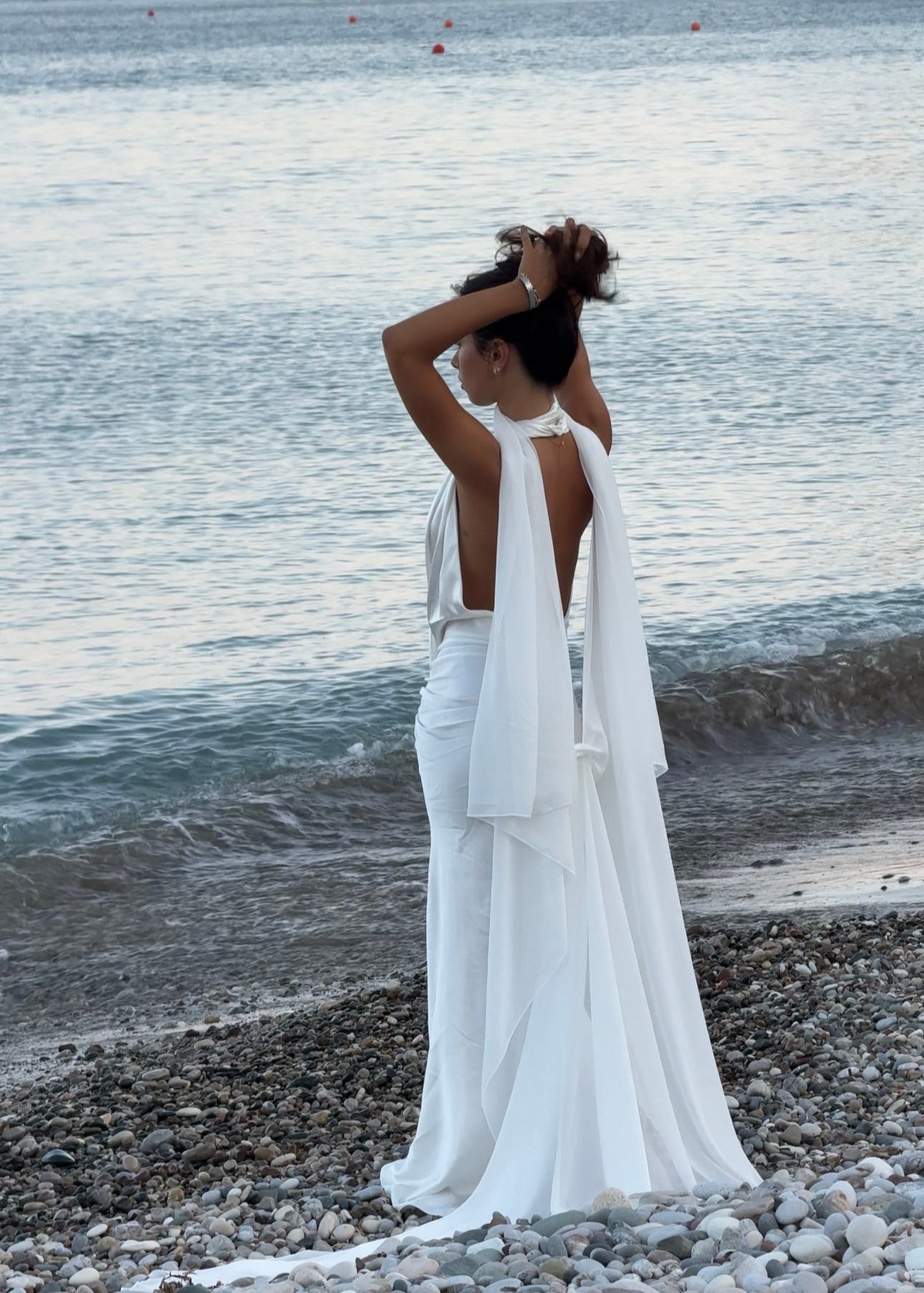 Woman in a white cape standing on a rocky beach with ocean view