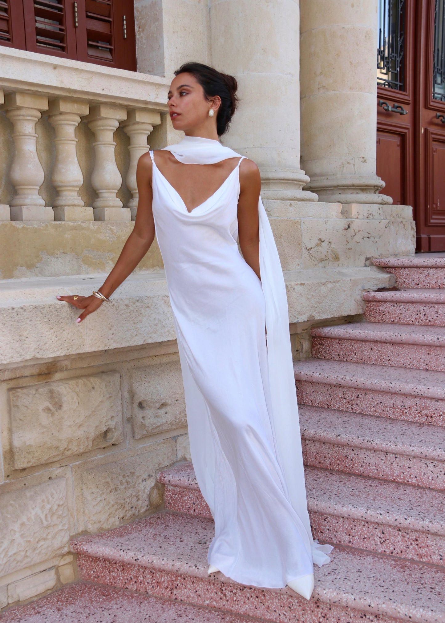 Woman in a white gown standing on stone steps with classical architecture in the background