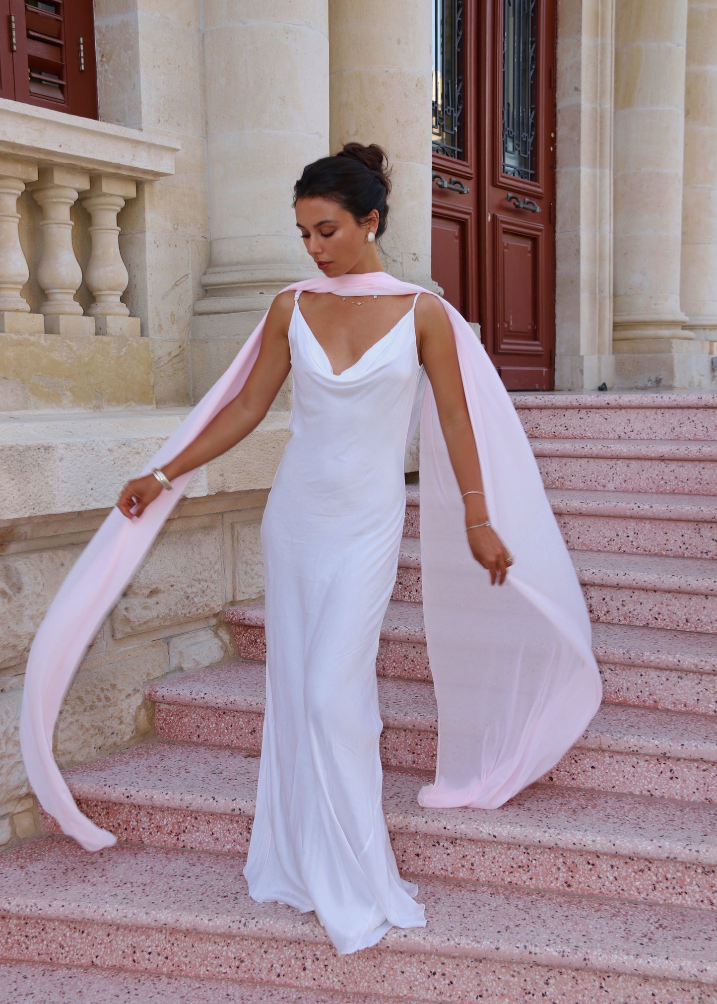 Woman in a white dress with a pink cape on stone steps of a building