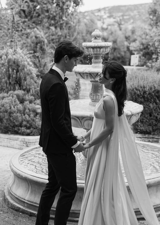 Black and white photo of a couple holding hands in front of a fountain.