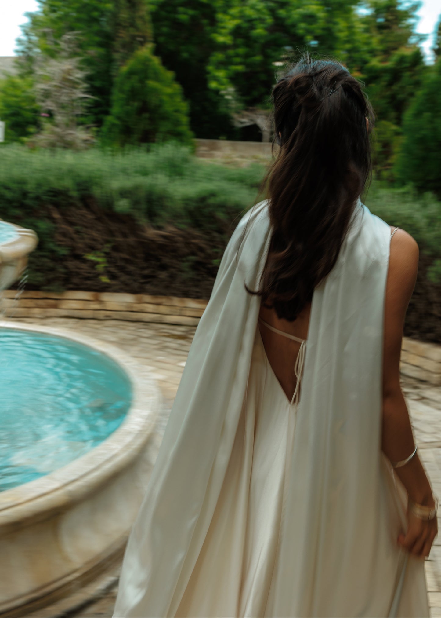 Woman in a white dress standing by a pool with greenery in the background
