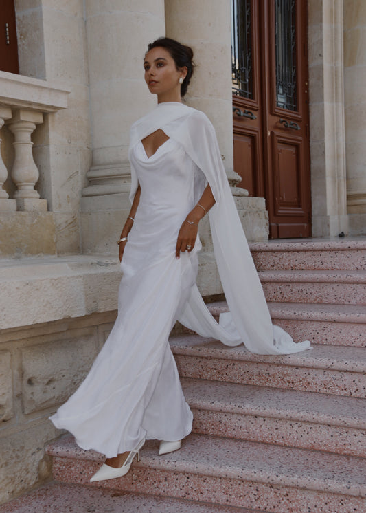 Woman in a white neck scarf and gown with a cape walking up stone steps.