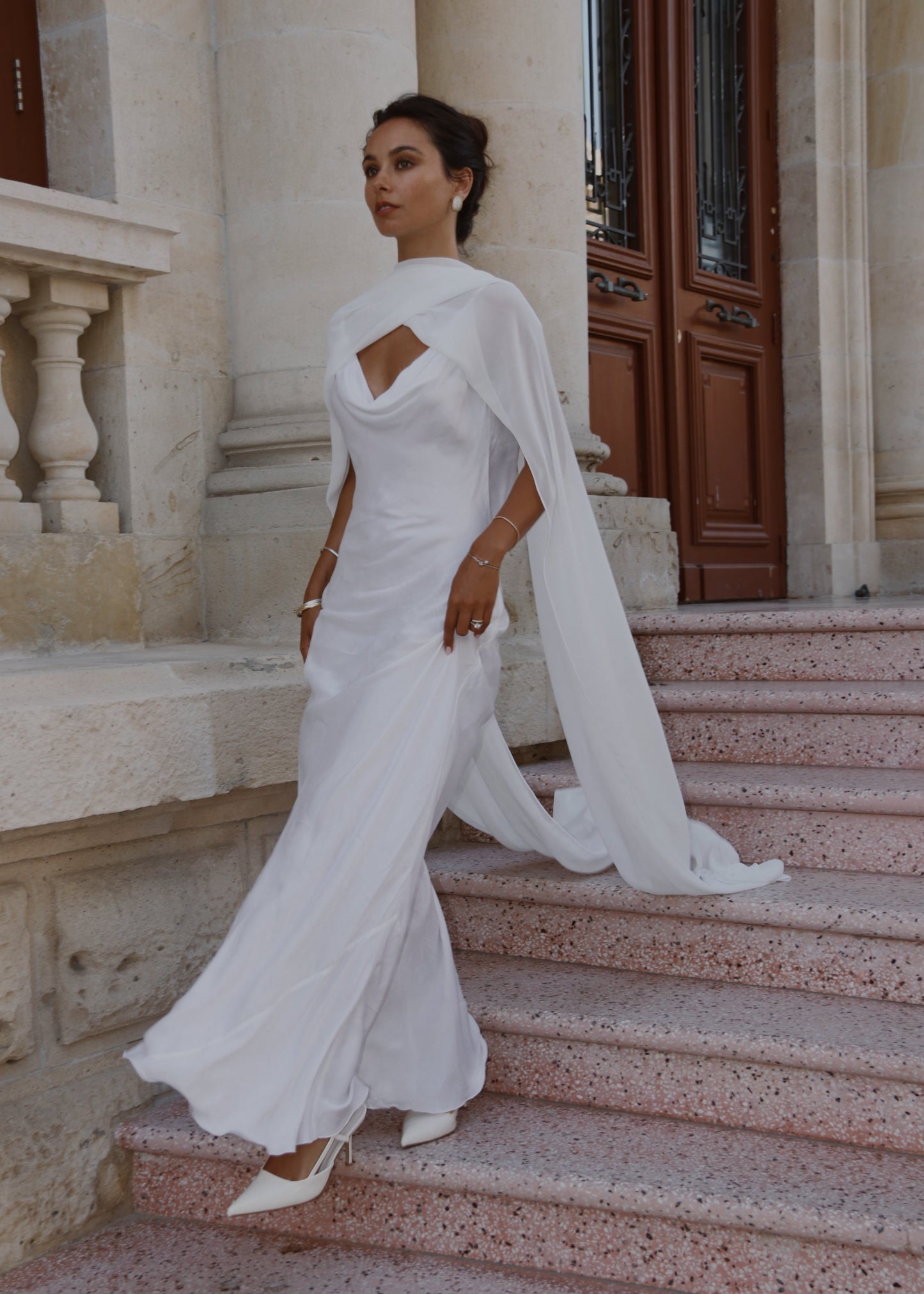 Woman in a white neck scarf and gown with a cape walking up stone steps.