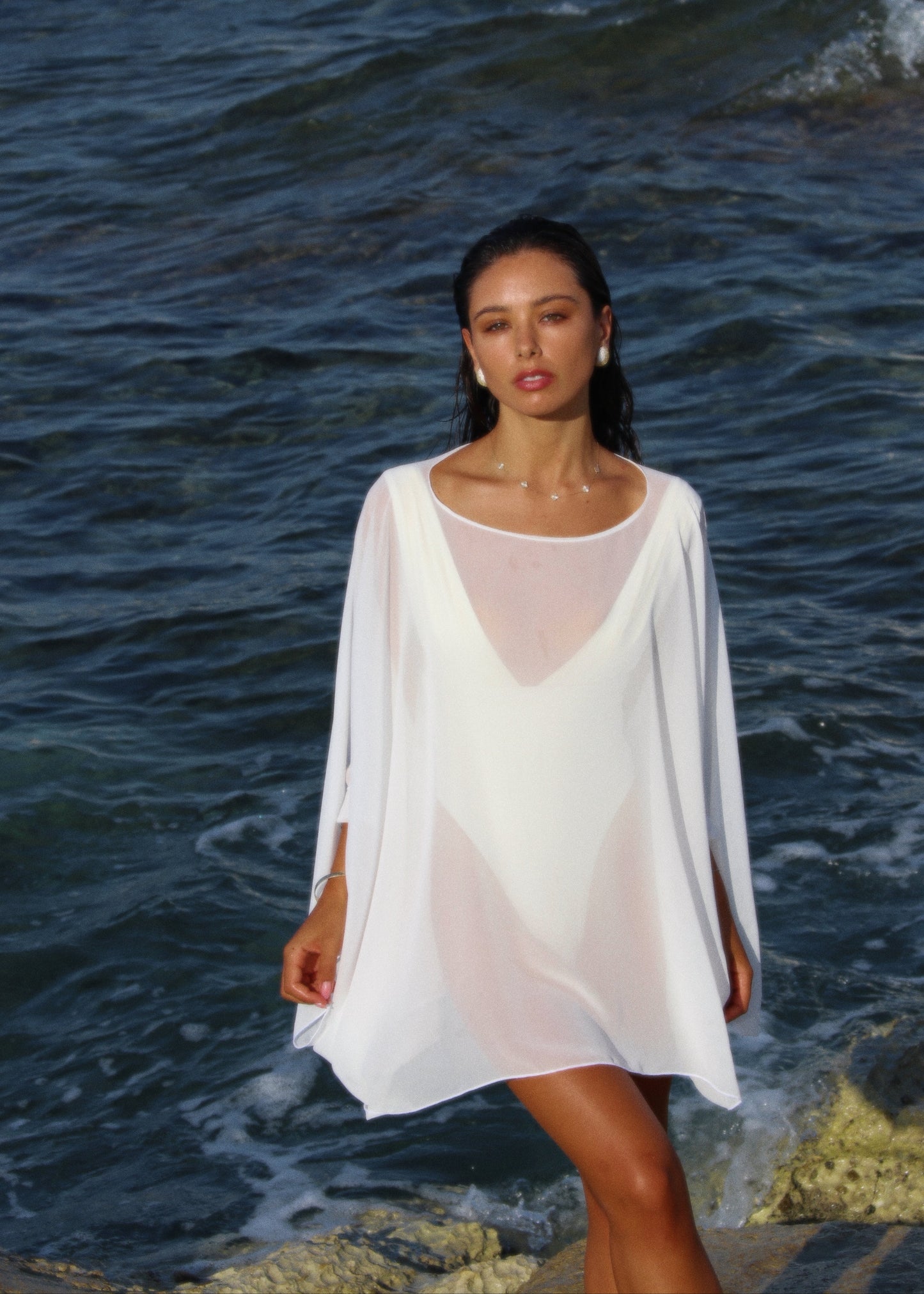 Woman in a white poncho standing by the ocean