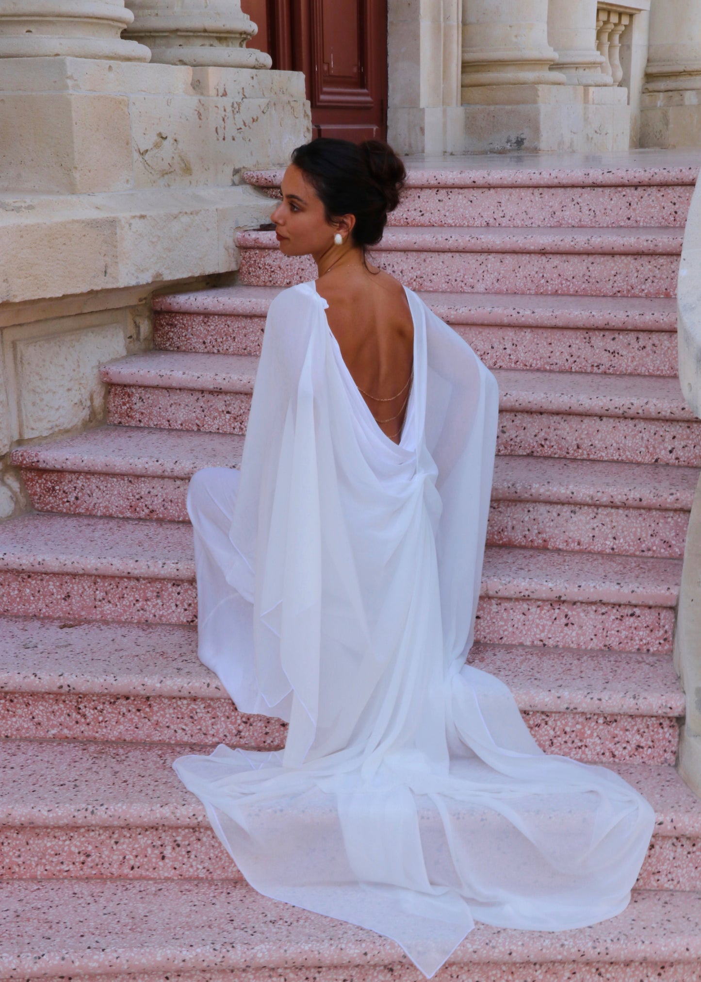 Woman in a white cape siting on stone steps of an elegant building