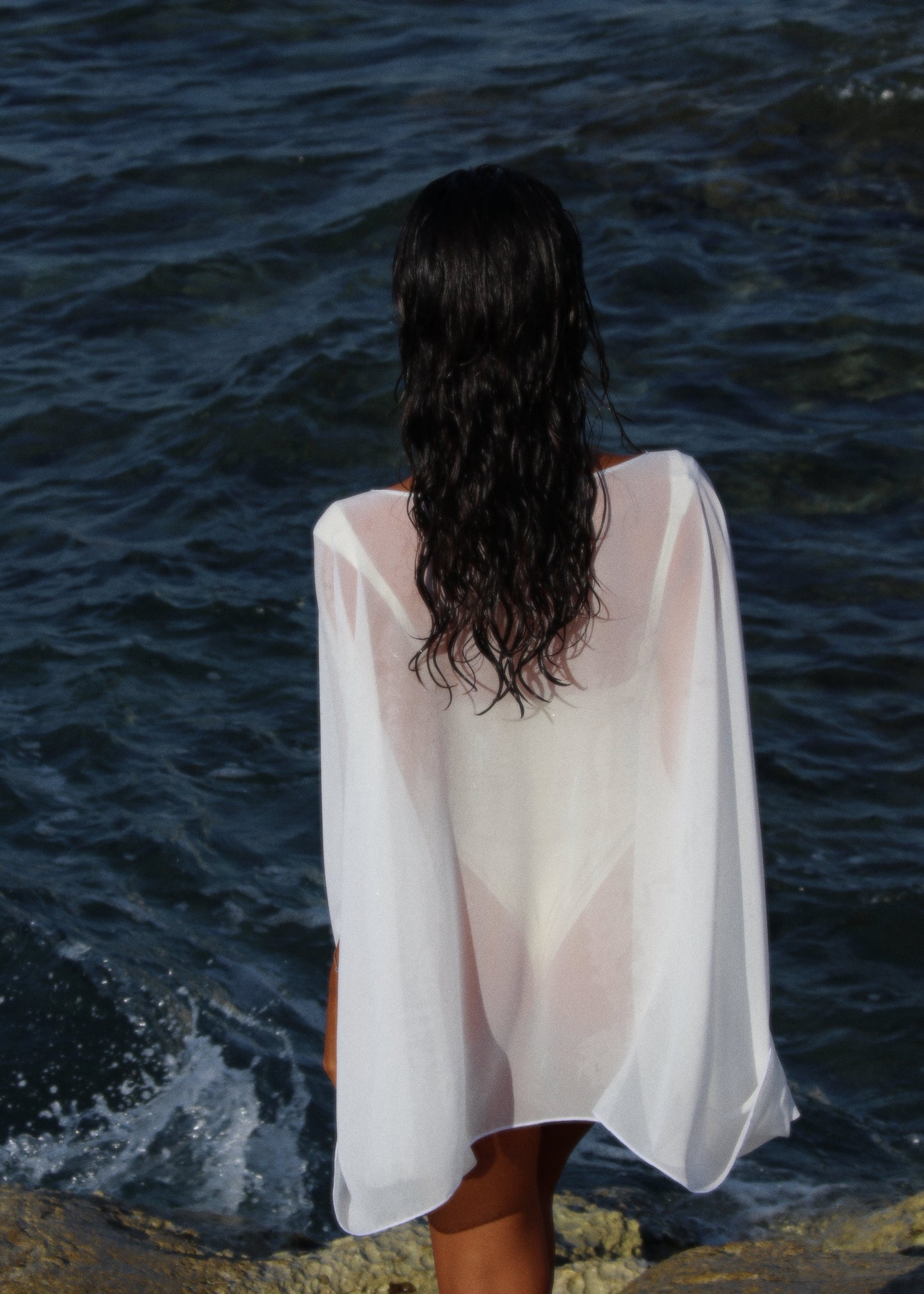 Person wearing a white sheer cover-up by the ocean