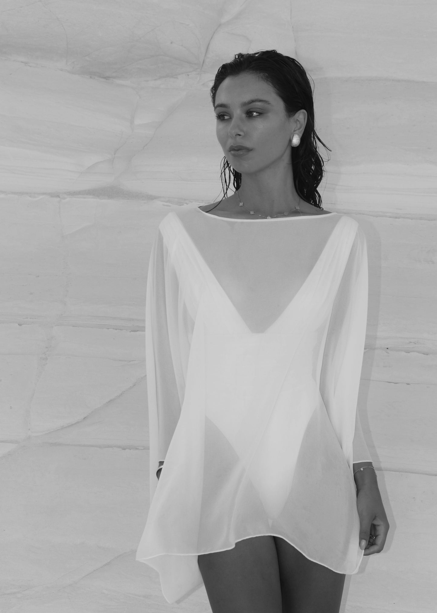 Woman wearing a white poncho with a deep neckline against a textured white background