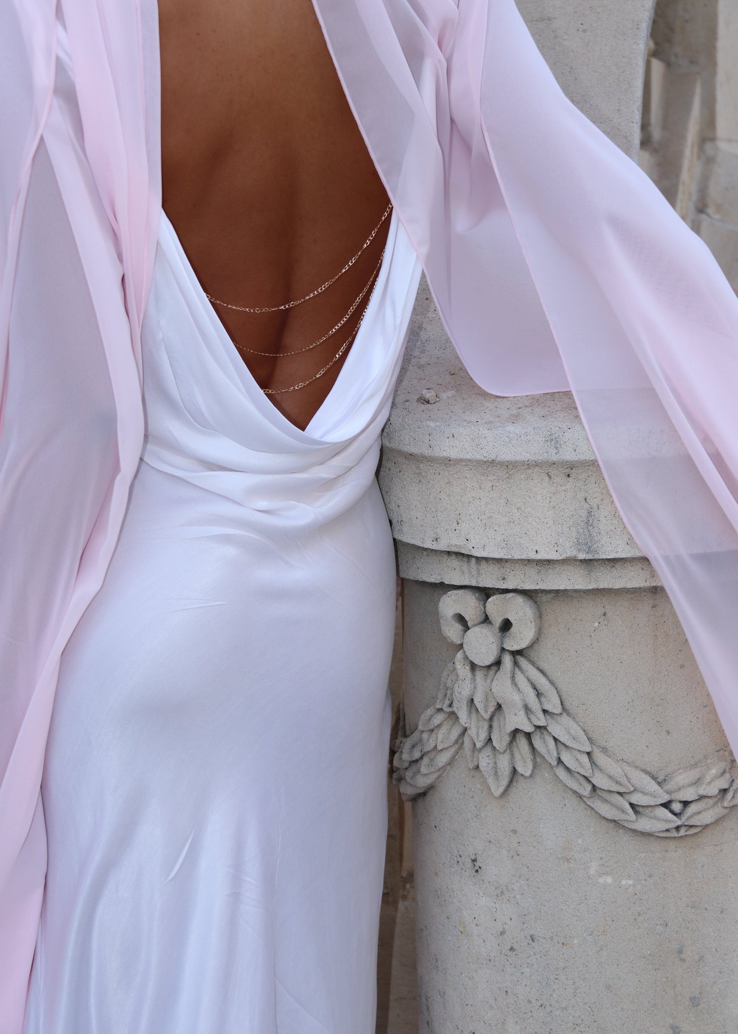 Close-up of a person wearing a light pink dress with a decorative belt on a stone surface.