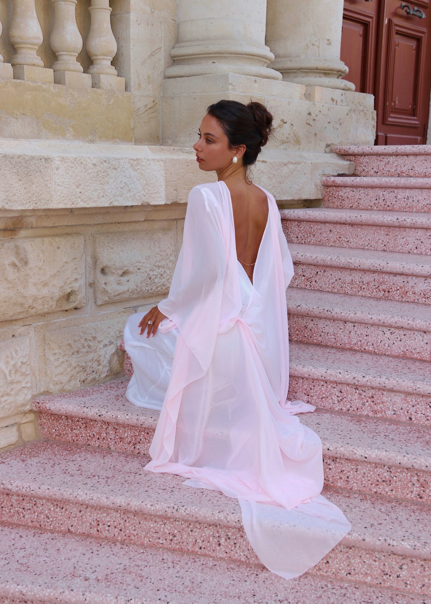 Woman in a pink cape sitting on stone steps outdoors