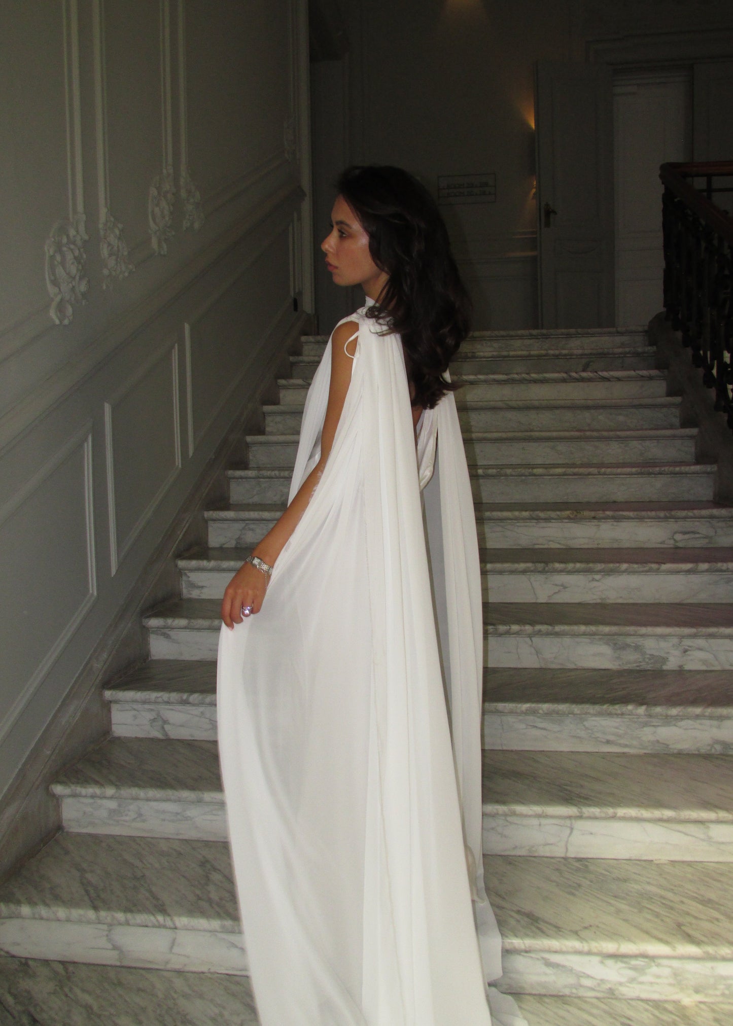 Woman in a white cape standing on a staircase with marble walls.