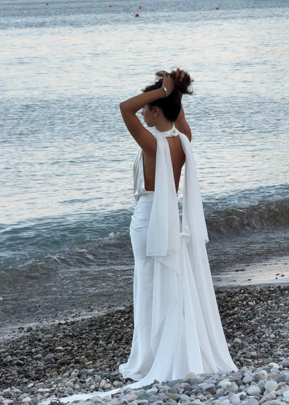 Woman in a white cape standing on a rocky beach with ocean view