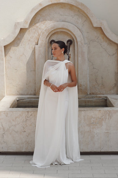 Woman in a white dress standing in front of a stone fountain.
