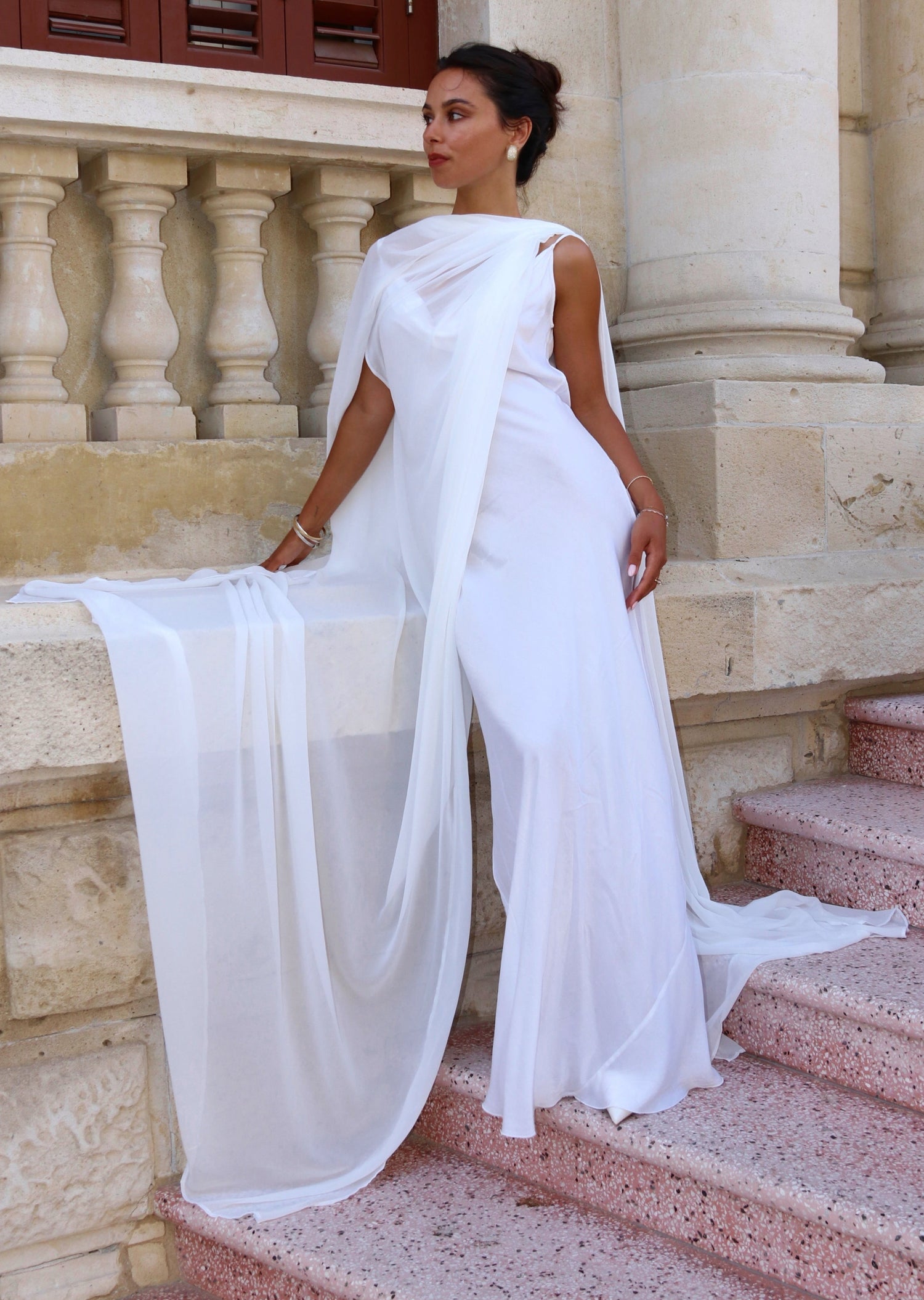 Woman in a white bridal cape standing on stone steps with classical architecture in the background