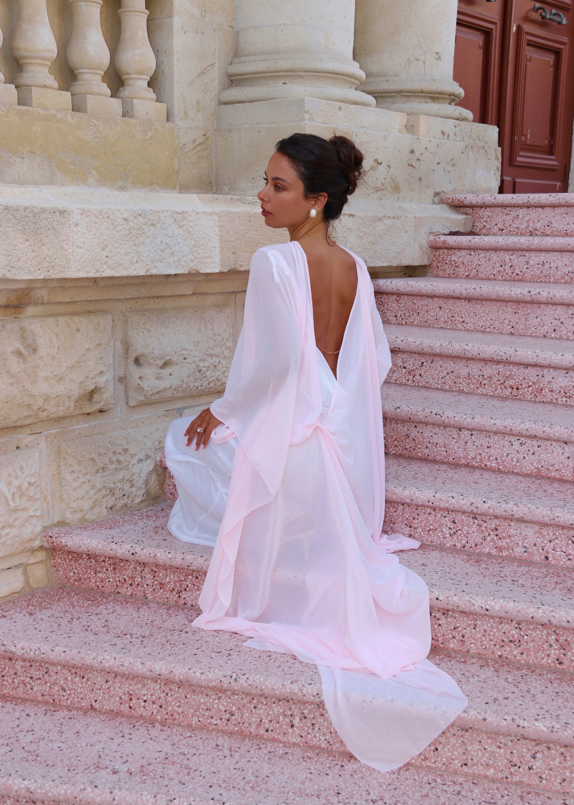 Woman in a pink cape sitting on stone steps outdoors